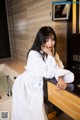 A woman in a white robe leaning on a counter.