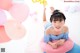 A little girl laying on a pink and blue pillow surrounded by balloons.