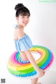 A young girl in a blue and white bathing suit holding a rainbow ring.