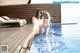 A woman in a white bathing suit sitting on the edge of a swimming pool.