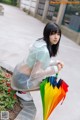 A woman in a white shirt holding a rainbow colored umbrella.