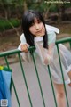 A woman in a white dress leaning against a green fence.