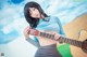 A woman holding a guitar in front of a blue sky.