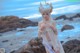 A woman in a white dress standing on a rocky beach.