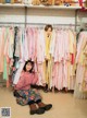 A woman sitting on the floor in front of a rack of clothes.