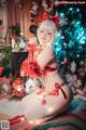 A woman in a red lingerie sitting on a rug in front of a Christmas tree.