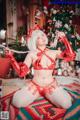 A woman in a red lingerie sitting on a rug in front of a Christmas tree.