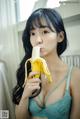 A woman in a blue bra holding a banana in her mouth.