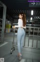 A woman in a white shirt and blue jeans standing next to a metal railing.