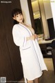 A woman in a white robe standing in a bathroom.