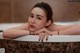 A woman laying in a bathtub with her hand on the edge of the tub.