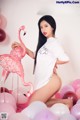 A woman in a white shirt is posing with a pink flamingo.