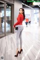 A woman in a red shirt and jeans standing in a hallway.