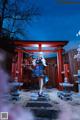 A woman in a blue and white dress standing in front of a red gate.