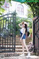 A woman standing in front of a gate with a hat on.