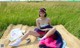 A woman sitting on a blanket in a field of tall grass.