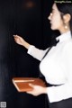 A woman in a white shirt and black skirt holding a book.