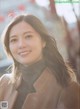 A woman in a brown coat smiles at the camera.