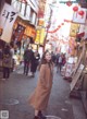 A woman in a brown coat is standing in the middle of a street.