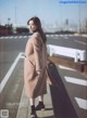 A woman in a beige coat is standing on a sidewalk.