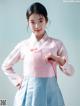 A woman in a pink and blue hanbok poses for a picture.