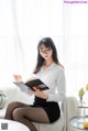 A woman sitting on a white couch reading a book.