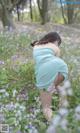 A woman in a blue dress crouching down in a field of flowers.