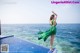 A woman in a green dress standing on the edge of a swimming pool.