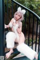 A woman in a white furry outfit is posing on a railing.