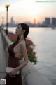 A woman in a red dress leaning against a wall by the water.