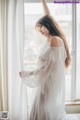 A woman in a white dress standing by a window.