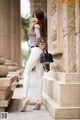 A woman leaning against a stone wall with a handbag.