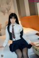 A woman in a school uniform sitting on a bed.