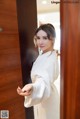 A woman in a white robe standing in front of a wooden door.