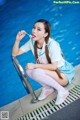 A woman sitting on the edge of a swimming pool eating a lollipop.