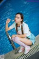 A woman sitting on the edge of a swimming pool holding a lollipop.