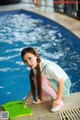 A woman in a sailor outfit crouching down next to a swimming pool.