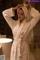 A woman in a white robe standing in a bathroom.