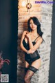 A woman in a black lingerie leaning against a brick wall.