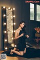 A woman in a black dress sitting on the floor in front of a mirror.