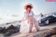 A woman in a white bikini and a straw hat on the beach.