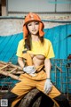 A woman in a yellow shirt and orange hard hat sitting on a tire.