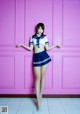 A woman in a sailor outfit posing in front of a pink wall.