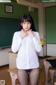 A woman in a white shirt and black pantyhose standing in front of a blackboard.