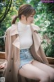 A woman sitting on a wooden bench wearing a trench coat.