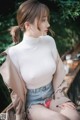 A woman sitting on a wooden bench wearing a white top and denim shorts.