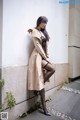 A woman in a trench coat leaning against a wall.