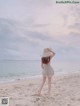 A woman in a white dress and straw hat standing on a beach.