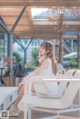 A woman sitting on a white chair in a white dress.