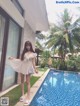 A woman standing next to a swimming pool in a white dress.